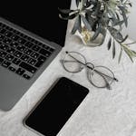Flat lay of a laptop, smartphone, glasses, and plant on a table.
